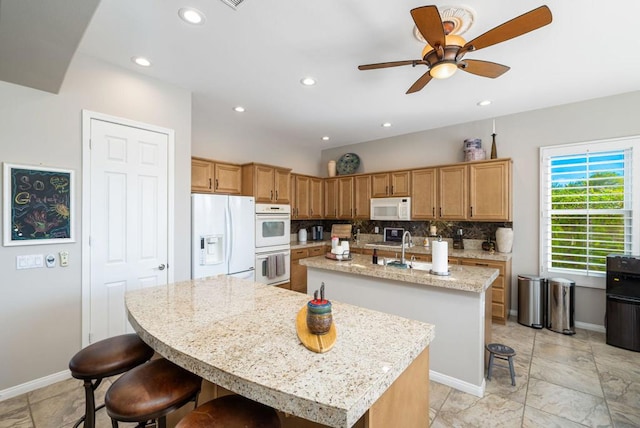 kitchen featuring white appliances, tasteful backsplash, a kitchen island with sink, ceiling fan, and a breakfast bar area