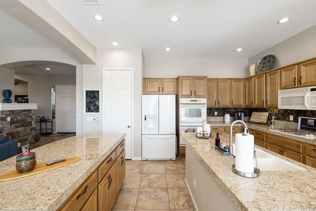 kitchen with decorative backsplash, light stone countertops, sink, and white appliances