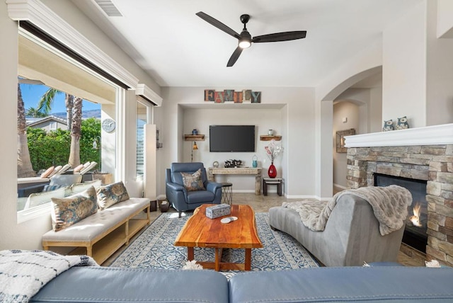 living room with ceiling fan and a stone fireplace