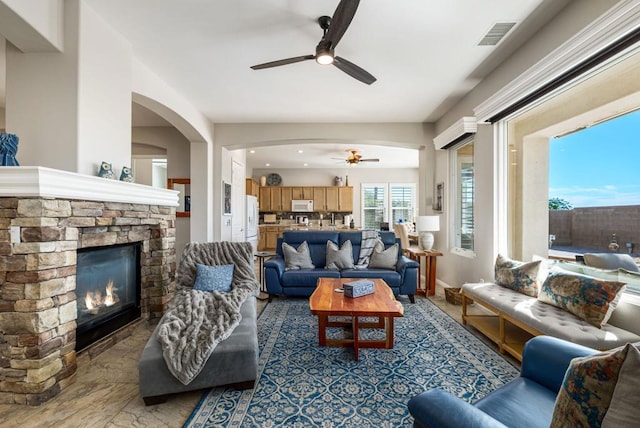 living room featuring ceiling fan and a stone fireplace