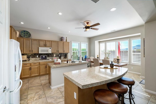 kitchen featuring a center island with sink, ceiling fan, backsplash, white appliances, and sink