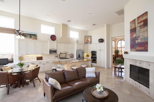 living room featuring a fireplace, a towering ceiling, ceiling fan, and sink