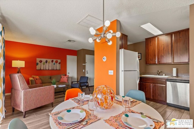 dining space with sink, light hardwood / wood-style floors, a textured ceiling, and an inviting chandelier