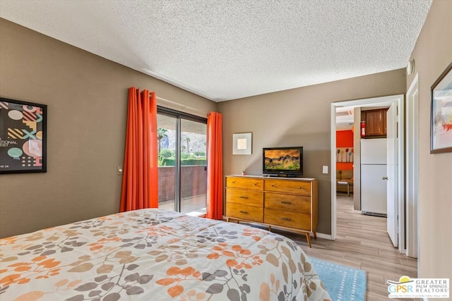 bedroom featuring access to exterior, light hardwood / wood-style flooring, white fridge, and a textured ceiling