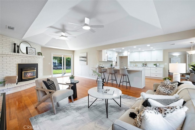 living room featuring a brick fireplace, light wood-type flooring, and ceiling fan