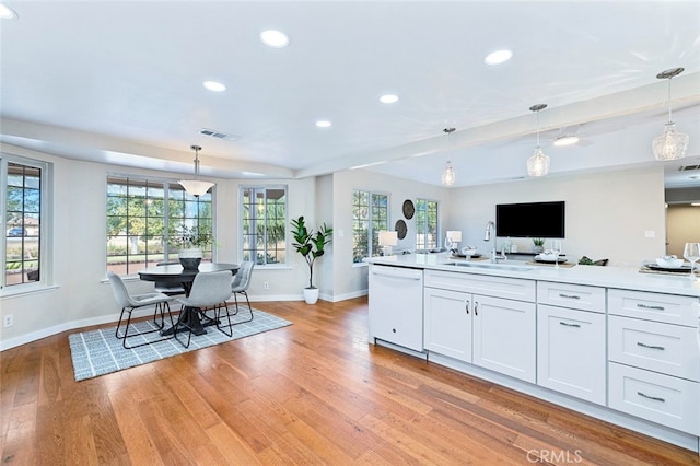 kitchen featuring hanging light fixtures, white dishwasher, light wood-type flooring, and white cabinets