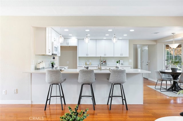 kitchen featuring a breakfast bar, white cabinetry, light hardwood / wood-style flooring, and pendant lighting