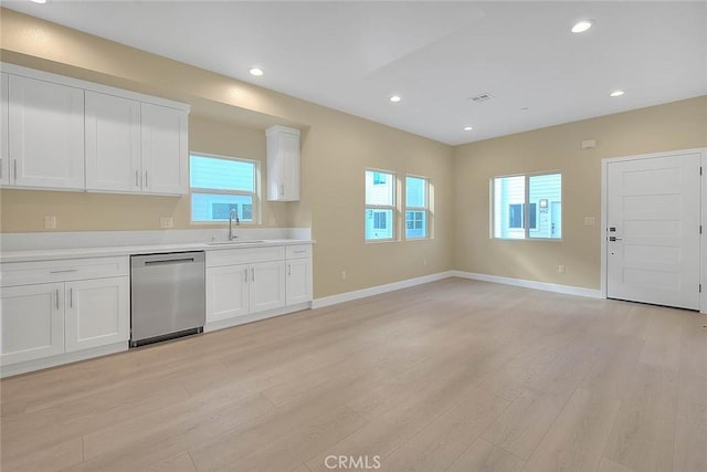 kitchen with stainless steel dishwasher, white cabinets, sink, and light hardwood / wood-style flooring