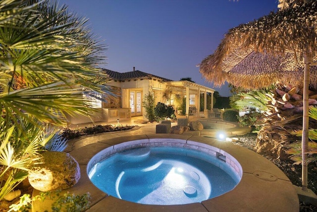 pool at dusk with an in ground hot tub and a patio area