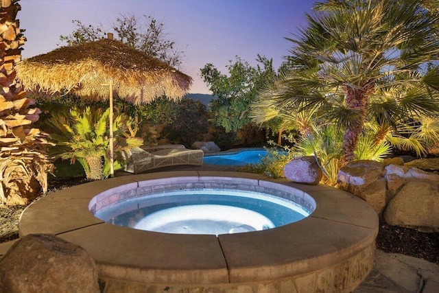 pool at dusk featuring an in ground hot tub