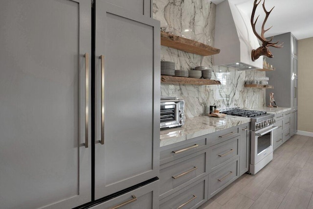 kitchen with gray cabinetry, wall chimney range hood, decorative backsplash, and high quality appliances