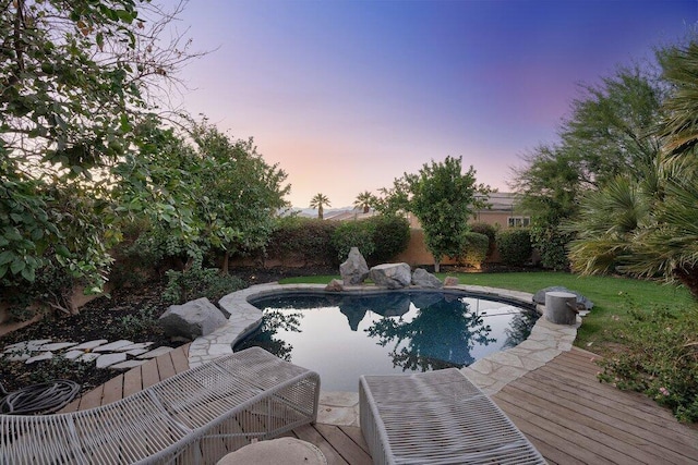 pool at dusk with a deck and a lawn