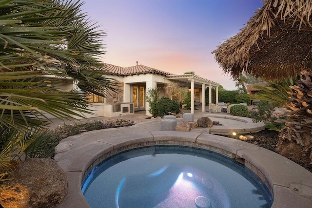 pool at dusk with a pergola, a patio area, and an in ground hot tub