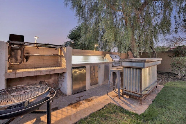 patio terrace at dusk featuring a grill and exterior kitchen