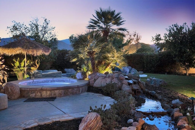 yard at dusk featuring an in ground hot tub, a mountain view, and a patio area