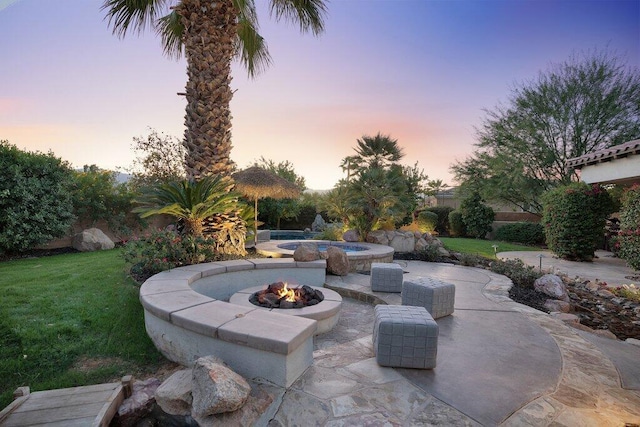 patio terrace at dusk featuring a lawn and a fire pit