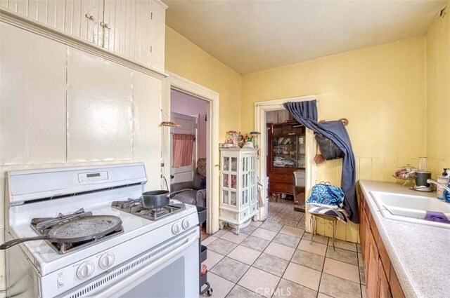 kitchen with sink, light tile patterned flooring, and white gas range oven