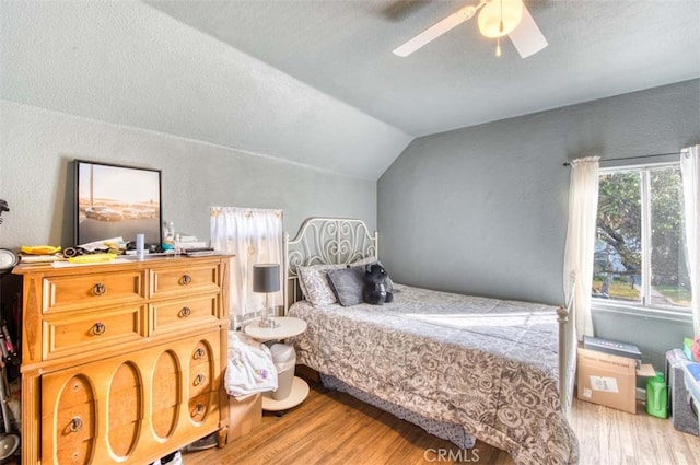 bedroom featuring vaulted ceiling, a textured ceiling, light hardwood / wood-style floors, and ceiling fan