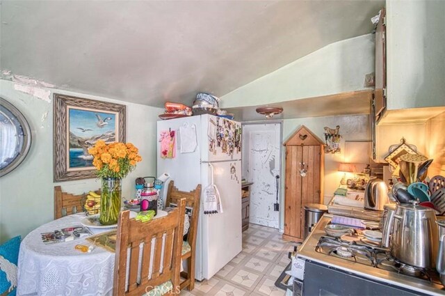 kitchen featuring stainless steel range oven, white fridge, and lofted ceiling