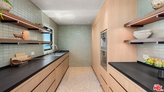 kitchen with stainless steel oven, light brown cabinetry, tasteful backsplash, and sink