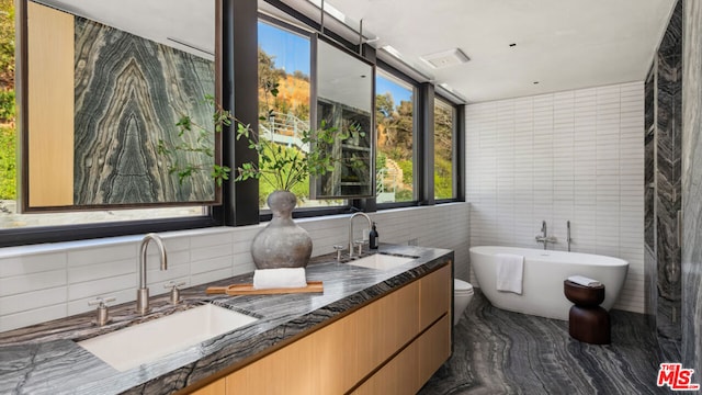 bathroom with vanity, a bath, tile walls, and toilet