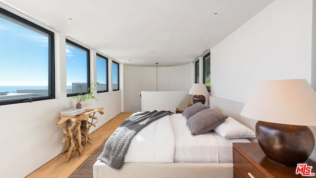 bedroom featuring light wood-type flooring, a water view, and expansive windows