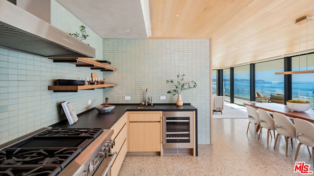 kitchen featuring wall chimney range hood, sink, tile walls, light brown cabinetry, and beverage cooler