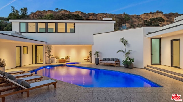 pool at dusk featuring a mountain view, an outdoor living space, and a patio