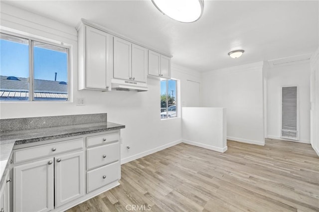 kitchen with white cabinetry, crown molding, light hardwood / wood-style floors, and dark stone counters