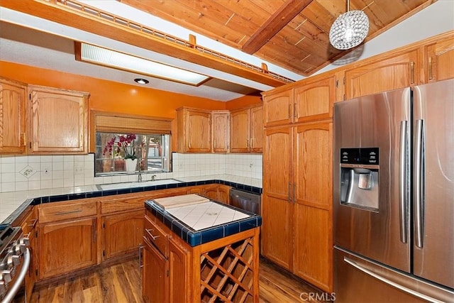 kitchen with tile counters, stainless steel appliances, vaulted ceiling with beams, light hardwood / wood-style floors, and a kitchen island