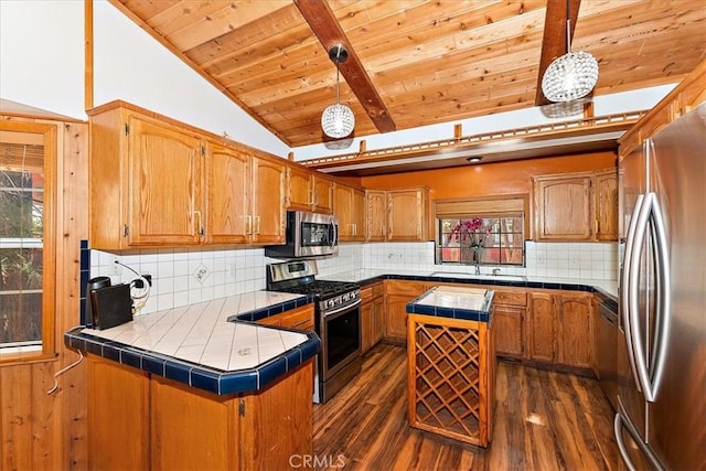 kitchen with hanging light fixtures, tile countertops, kitchen peninsula, and stainless steel appliances