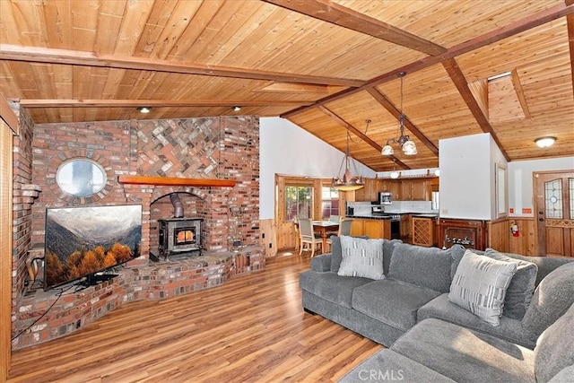 living room with wood walls, wooden ceiling, a wood stove, light hardwood / wood-style flooring, and beamed ceiling