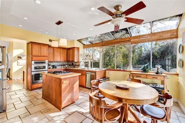 kitchen with a center island, hanging light fixtures, ceiling fan, appliances with stainless steel finishes, and tasteful backsplash