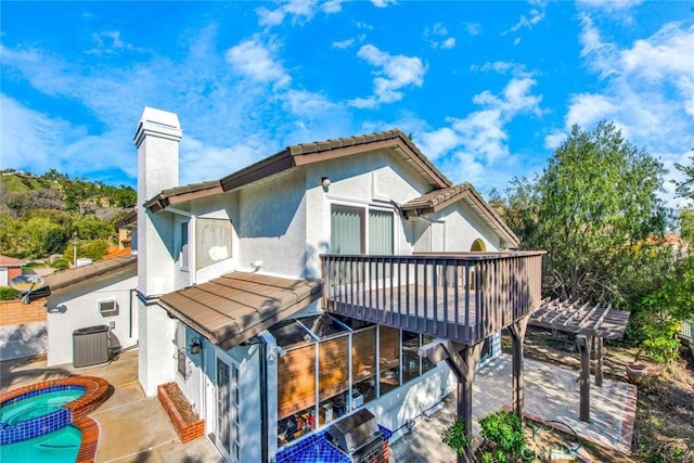 back of property with a balcony, an in ground hot tub, and a patio