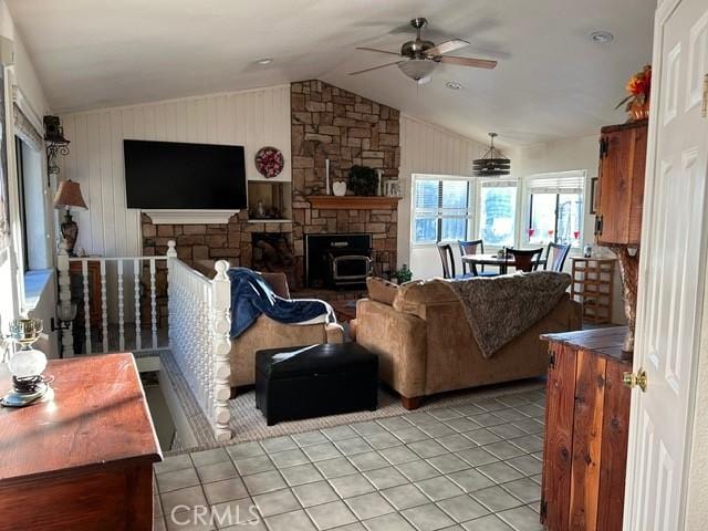 living room featuring a wood stove, wooden walls, vaulted ceiling, ceiling fan, and light tile patterned floors