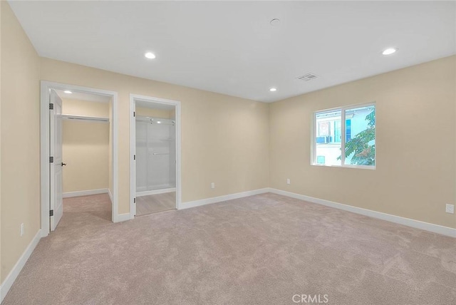 unfurnished bedroom with a walk in closet, light carpet, and a closet