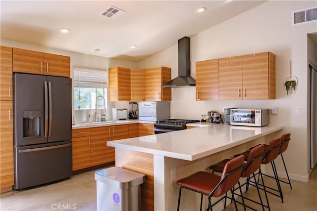 kitchen featuring sink, wall chimney exhaust hood, a kitchen bar, kitchen peninsula, and stainless steel appliances