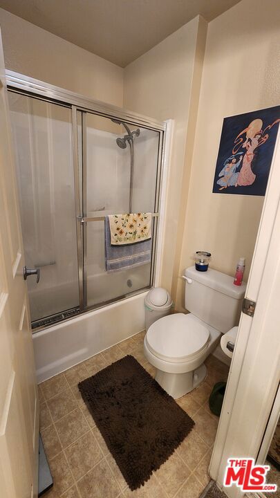 bathroom featuring tile patterned flooring, toilet, and combined bath / shower with glass door