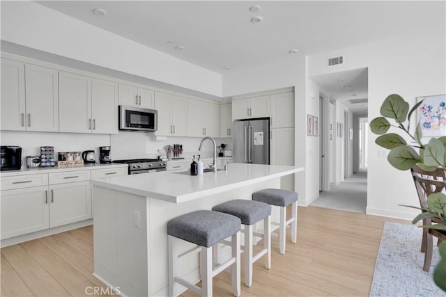 kitchen with white cabinetry, an island with sink, appliances with stainless steel finishes, and light hardwood / wood-style flooring