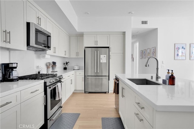 kitchen with appliances with stainless steel finishes, light hardwood / wood-style flooring, white cabinetry, and sink