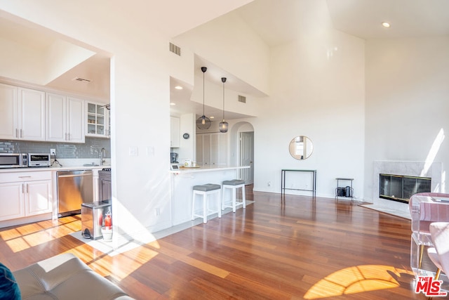 kitchen with light wood-type flooring, backsplash, stainless steel appliances, white cabinets, and a high ceiling