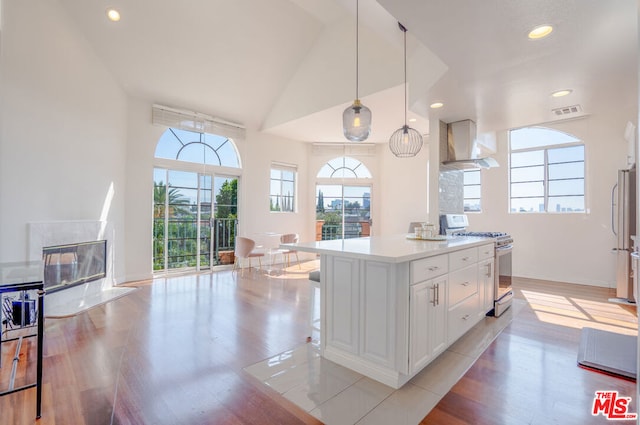 kitchen featuring white cabinetry, wall chimney exhaust hood, hanging light fixtures, light hardwood / wood-style flooring, and white range with gas stovetop