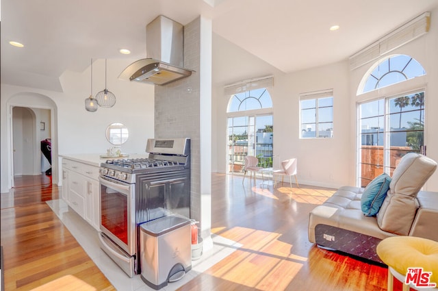 kitchen featuring gas range, light hardwood / wood-style floors, white cabinetry, and range hood