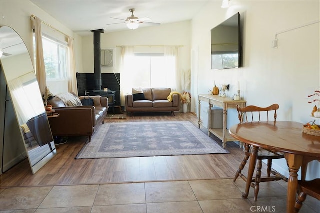 tiled living room with ceiling fan, lofted ceiling, and a wood stove