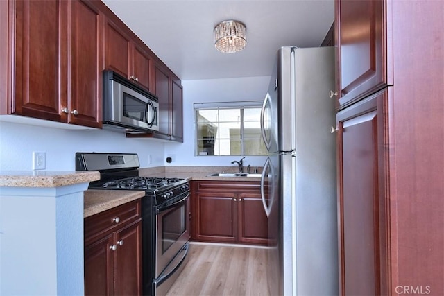 kitchen featuring sink, stainless steel appliances, an inviting chandelier, light stone counters, and light hardwood / wood-style floors