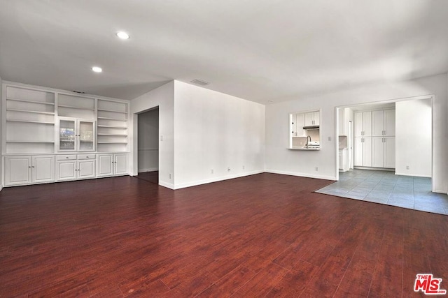 unfurnished living room featuring built in features and dark hardwood / wood-style floors