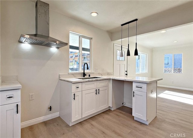 kitchen with kitchen peninsula, white cabinetry, sink, and wall chimney exhaust hood