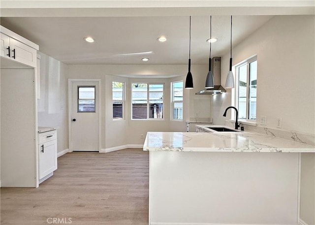 kitchen with kitchen peninsula, white cabinetry, hanging light fixtures, and wall chimney range hood