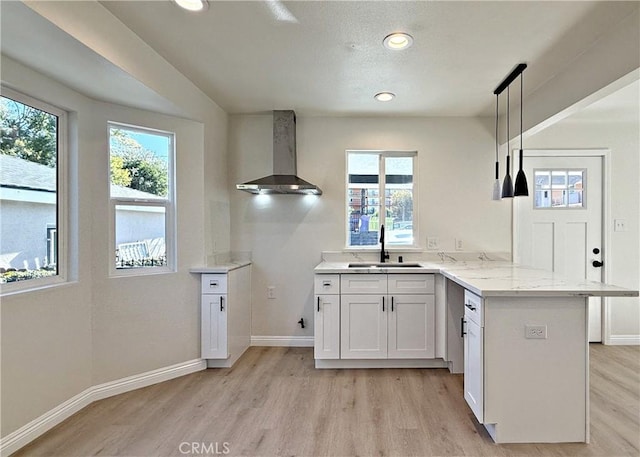 kitchen with light stone counters, sink, wall chimney range hood, pendant lighting, and white cabinetry