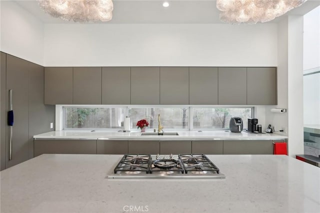 kitchen with sink, light stone countertops, stainless steel gas cooktop, and gray cabinetry